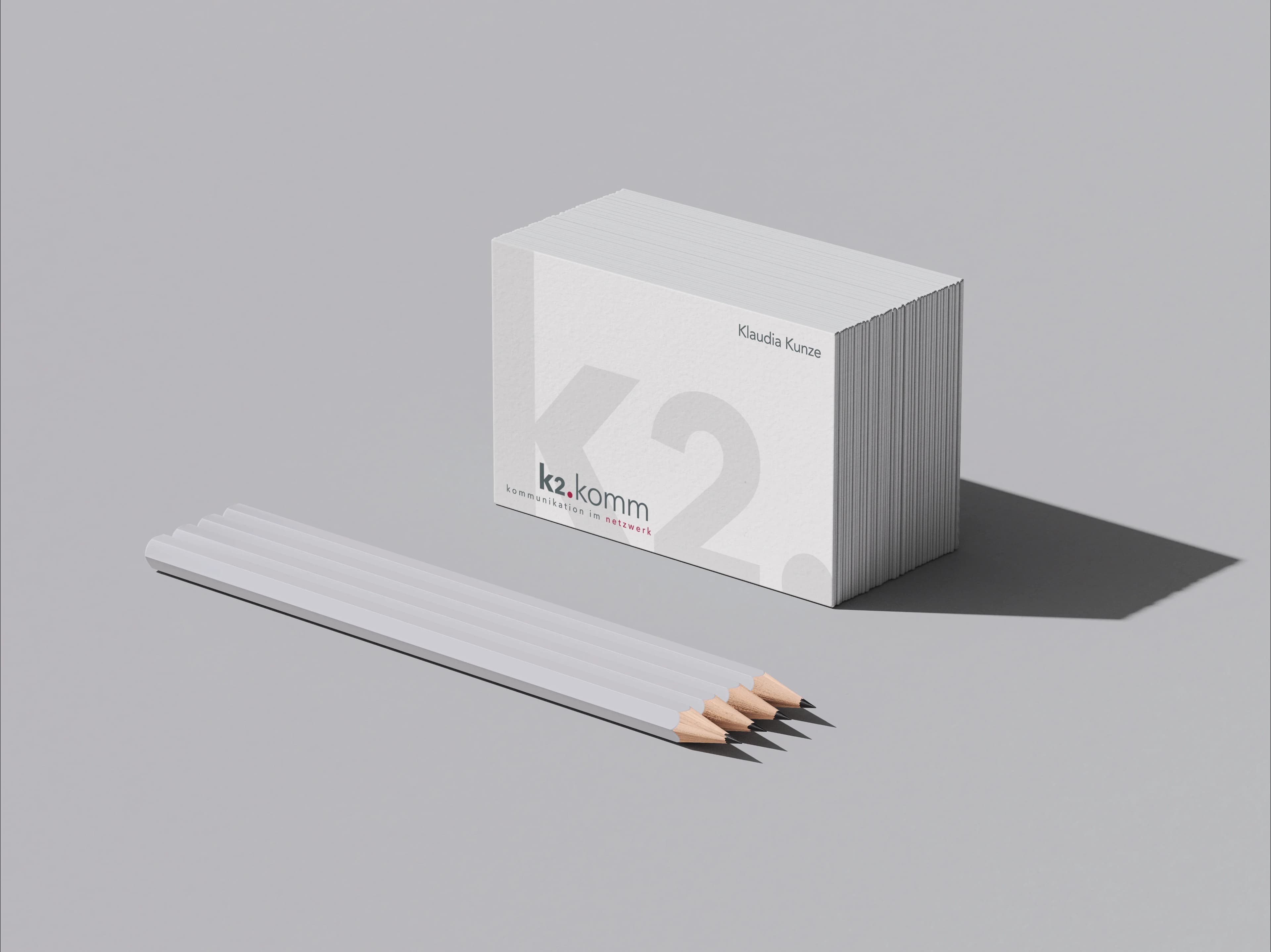 k2.komm business card stack and white pencils on a grey ground